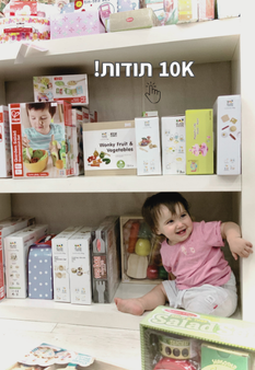 פעוטה יושבת לצד משחקים בתוך מדף רצפתי בחנות